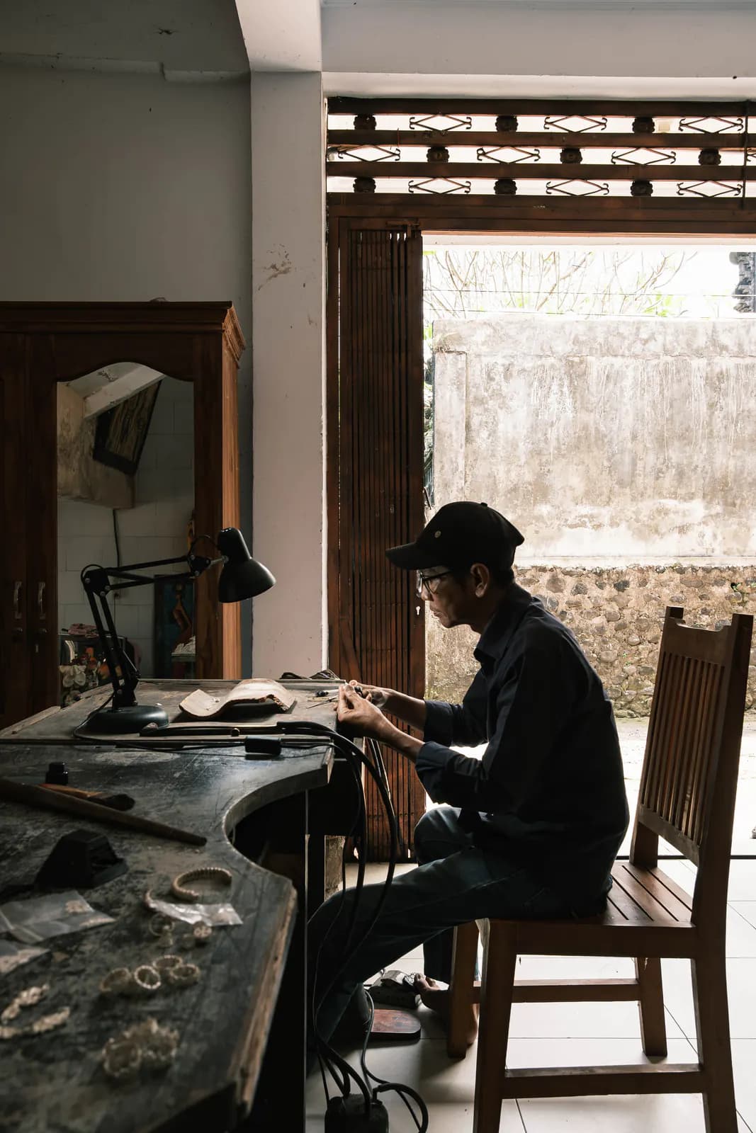 Artisan seated at a curved wooden workbench by an open doorway in the studio