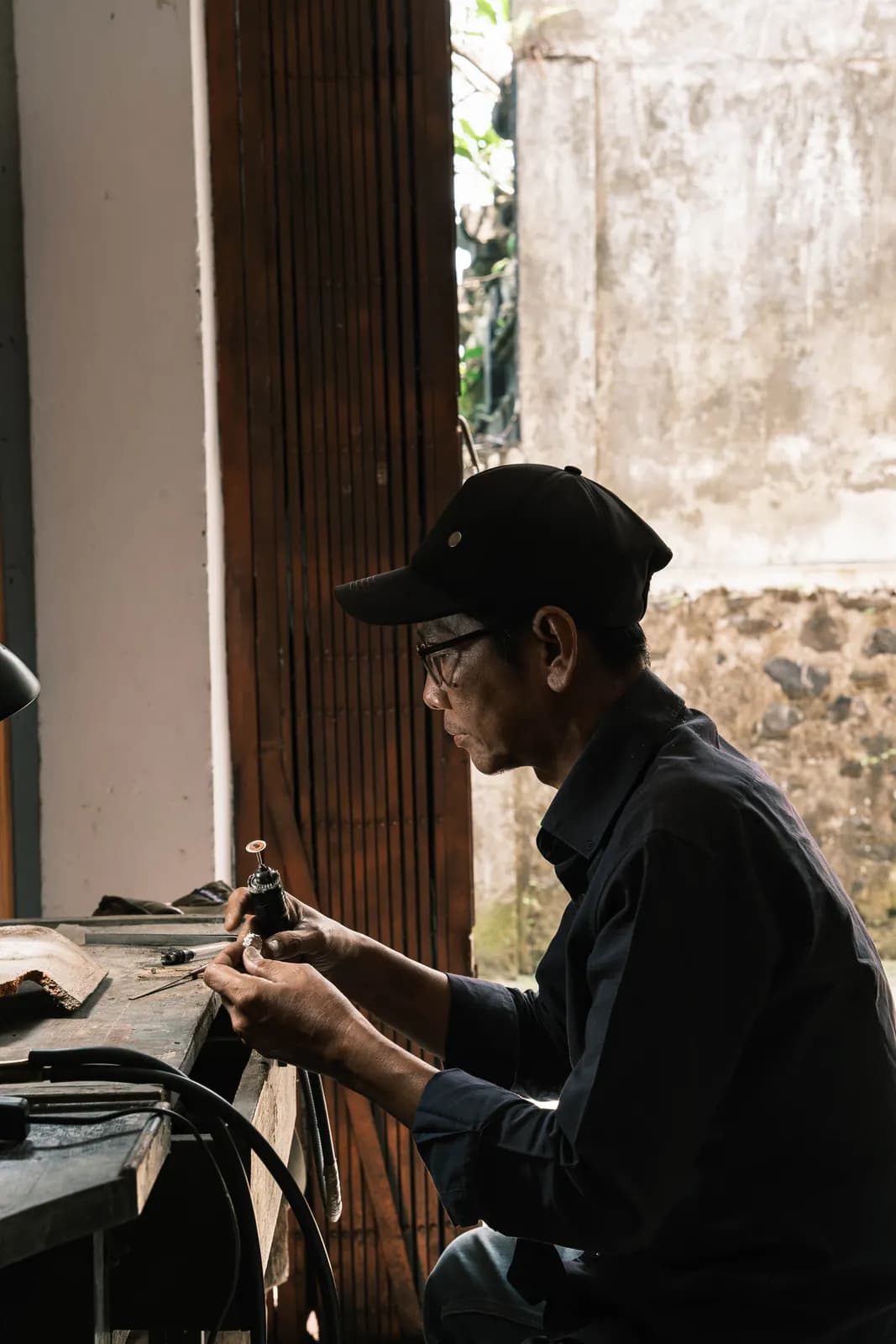 Artisan in a black cap and glasses working on a piece at the bench