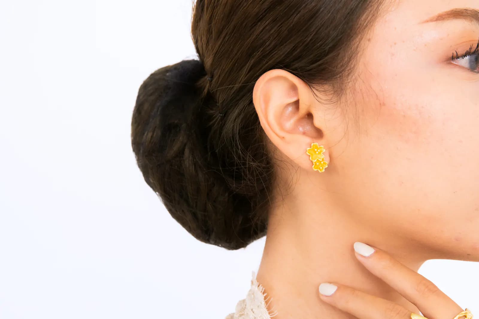 Ear close-up of a model with a hair bun wearing a gold flower stud