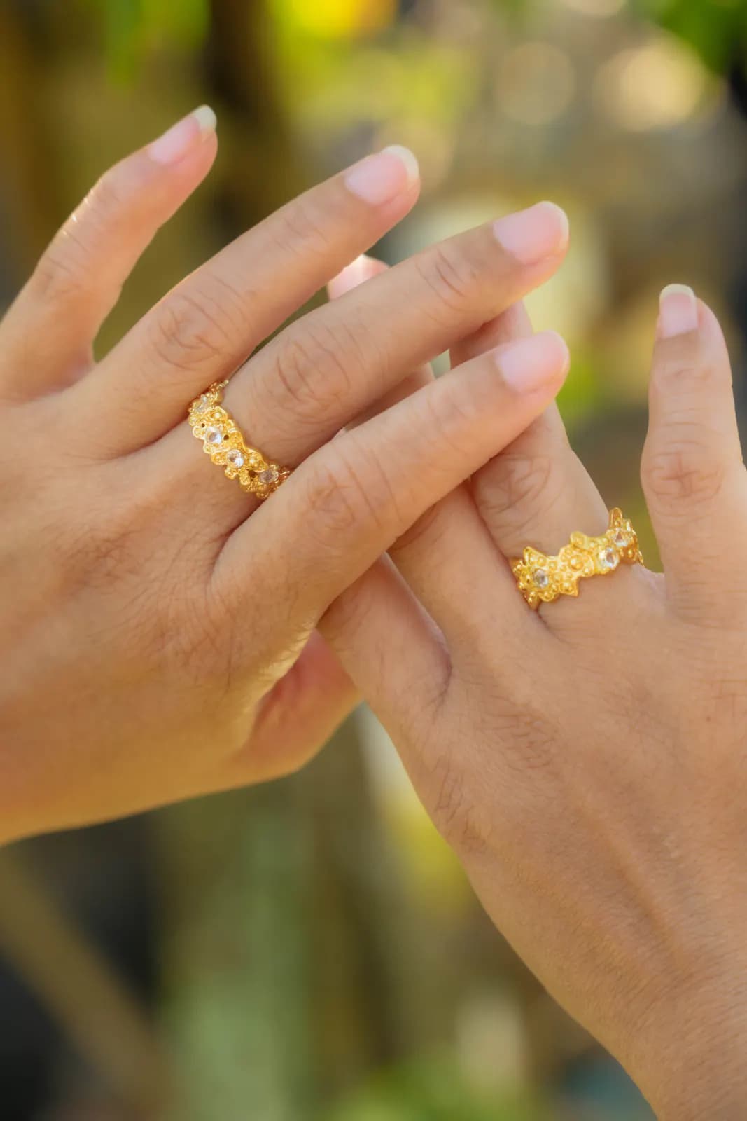 Hands with two gold floral rings against blurred green foliage