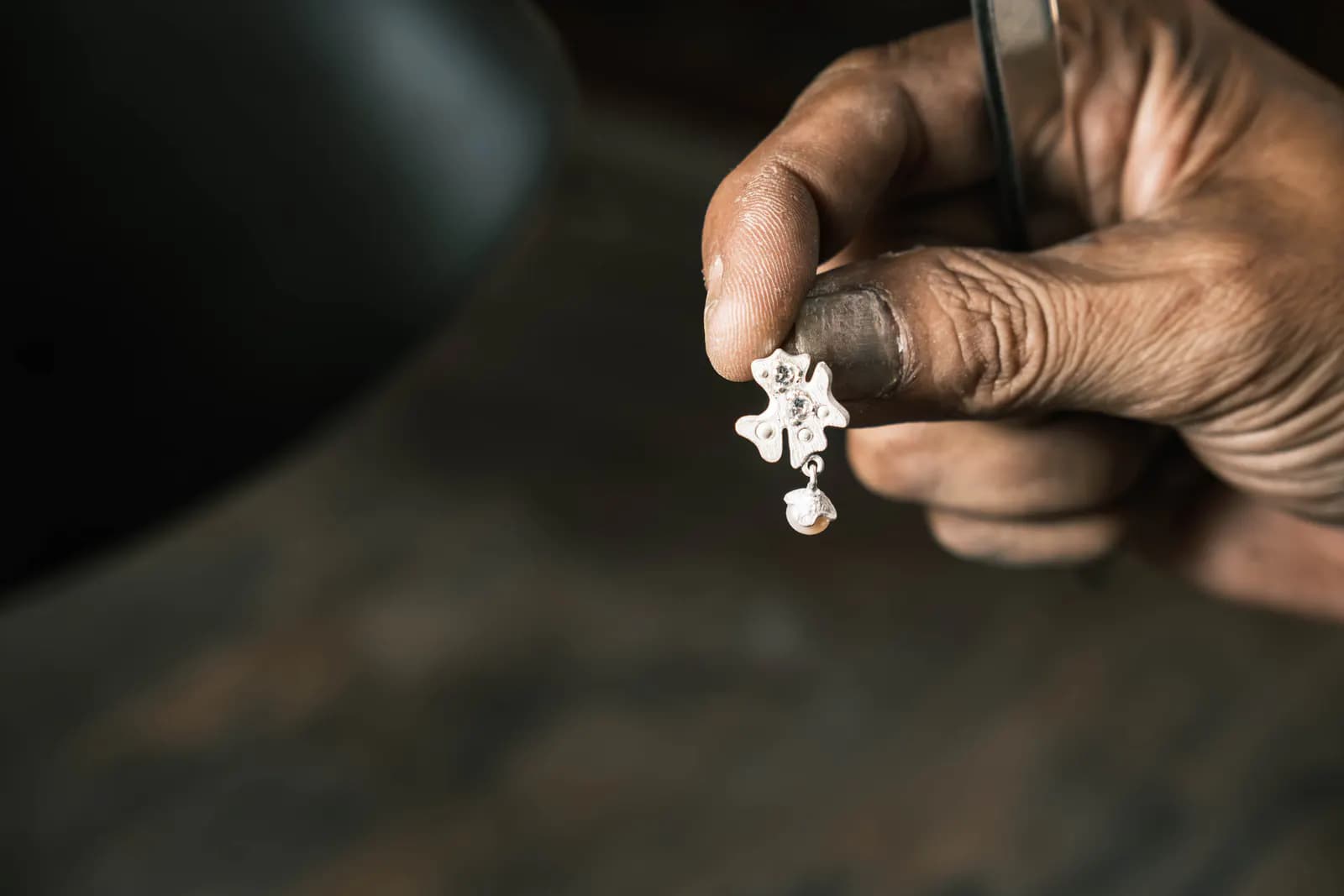 Fingers holding a flower charm with a pearl drop against a dark background