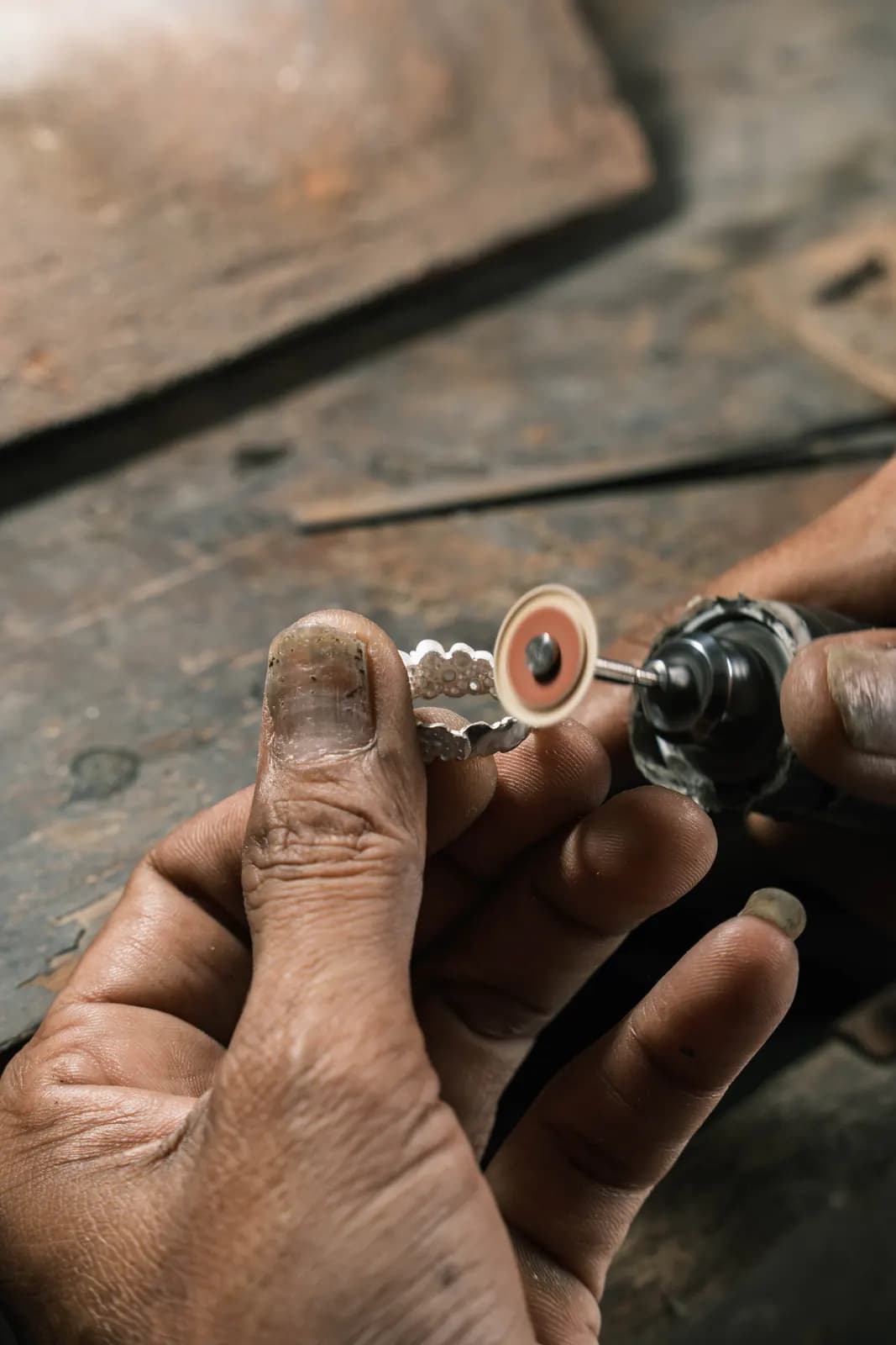 Hands polishing a ring with a rotary disc over a dark wooden bench