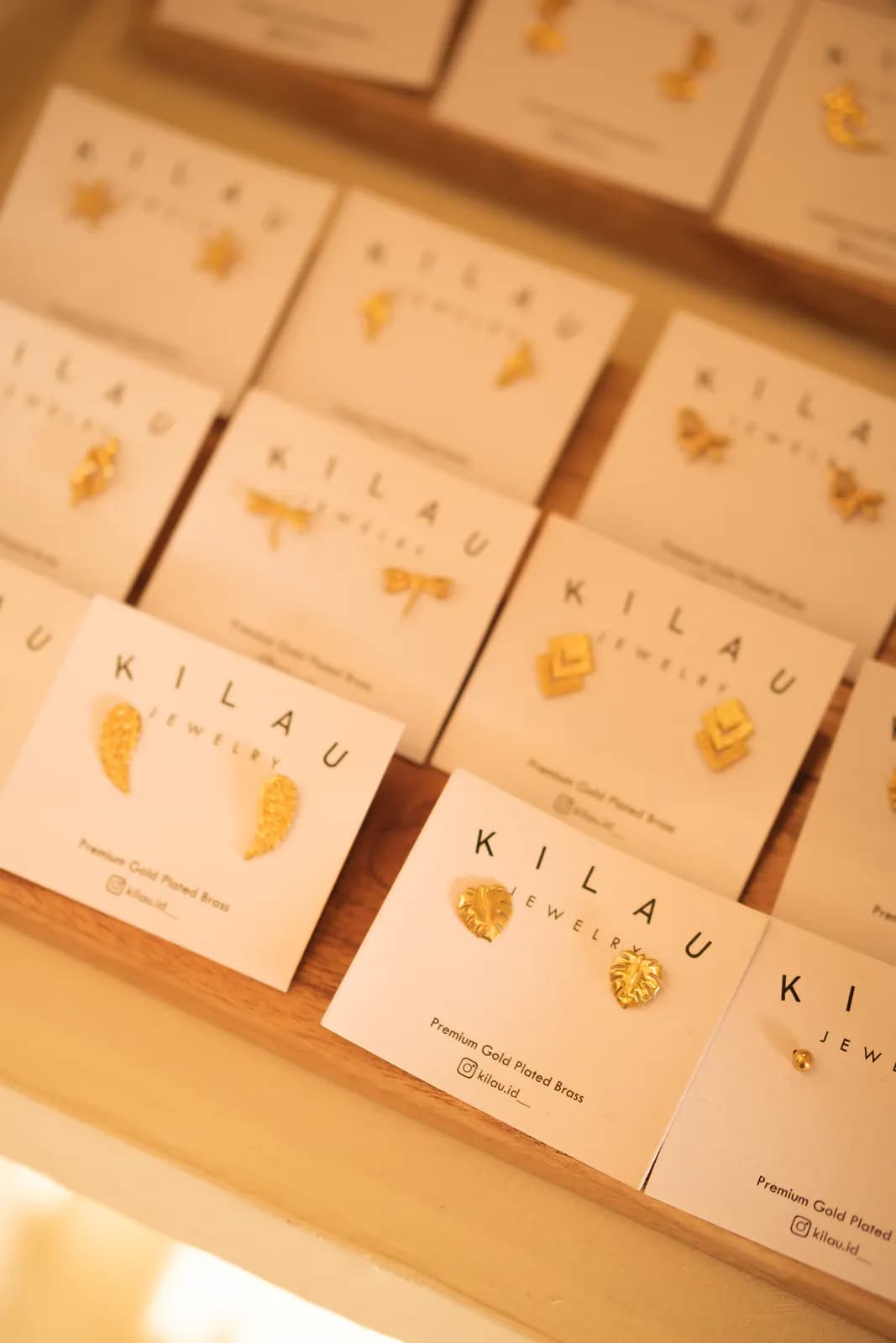 Rows of KILAU earring cards with gold studs on a wooden tray