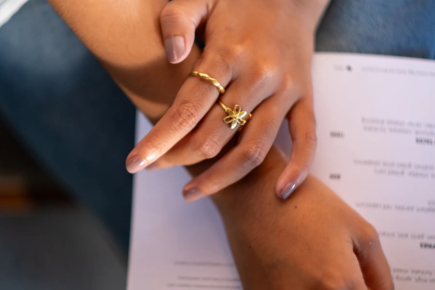 Crossed hands wearing KILAU gold rings resting on a café menu