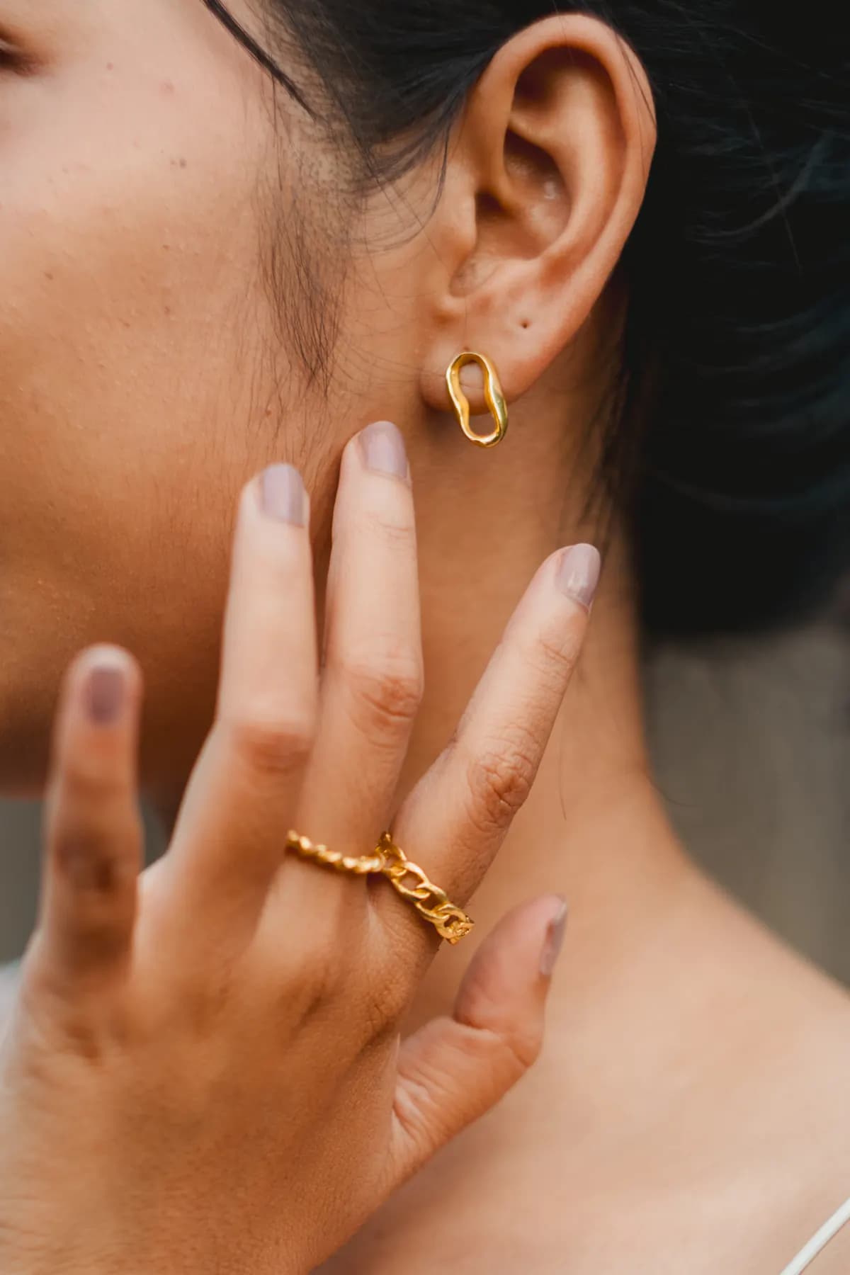 Hand with chain rings raised to the jaw beside a gold link earring