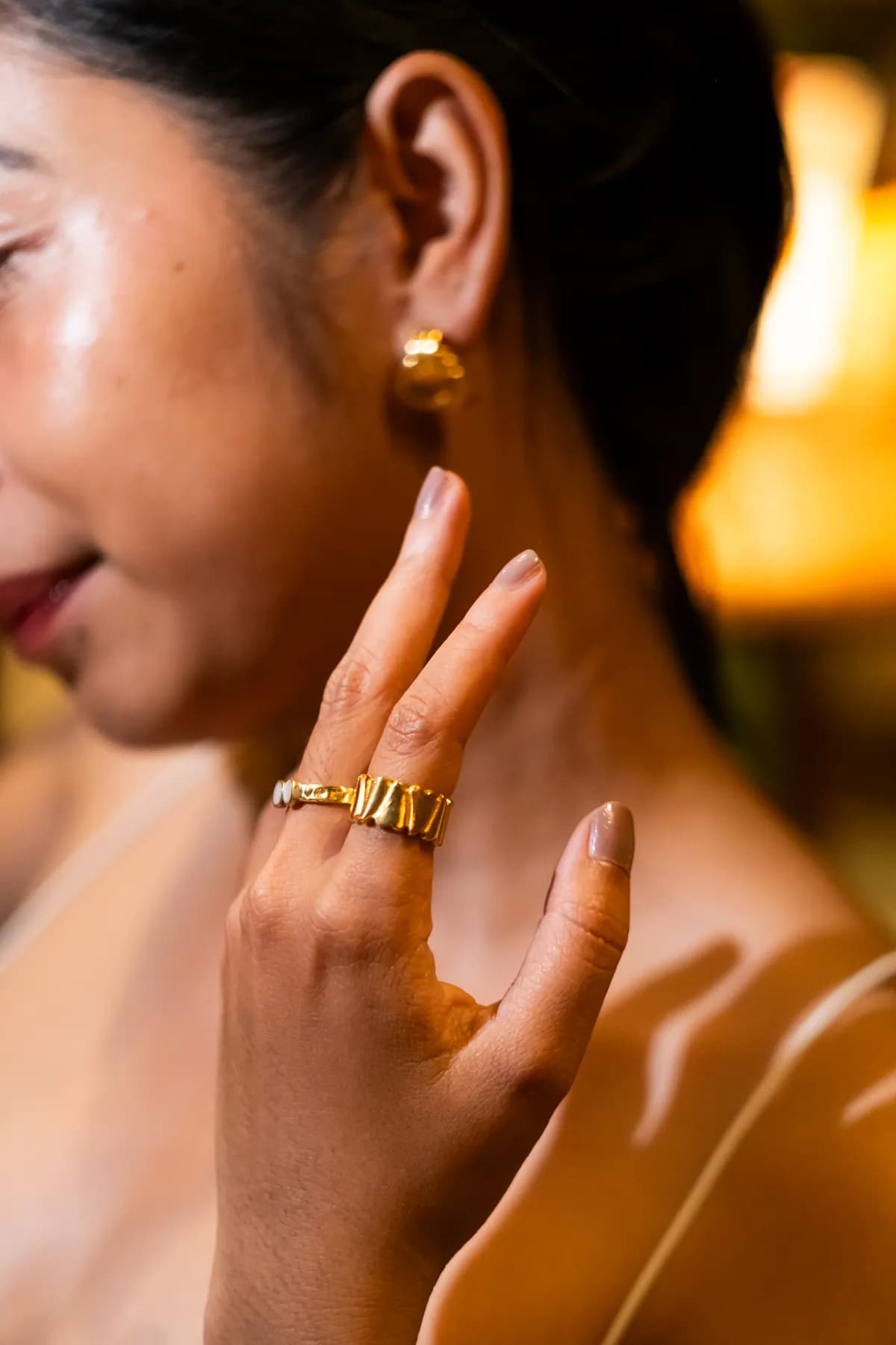 Smiling profile with a gold dome earring and stacked rings in warm light
