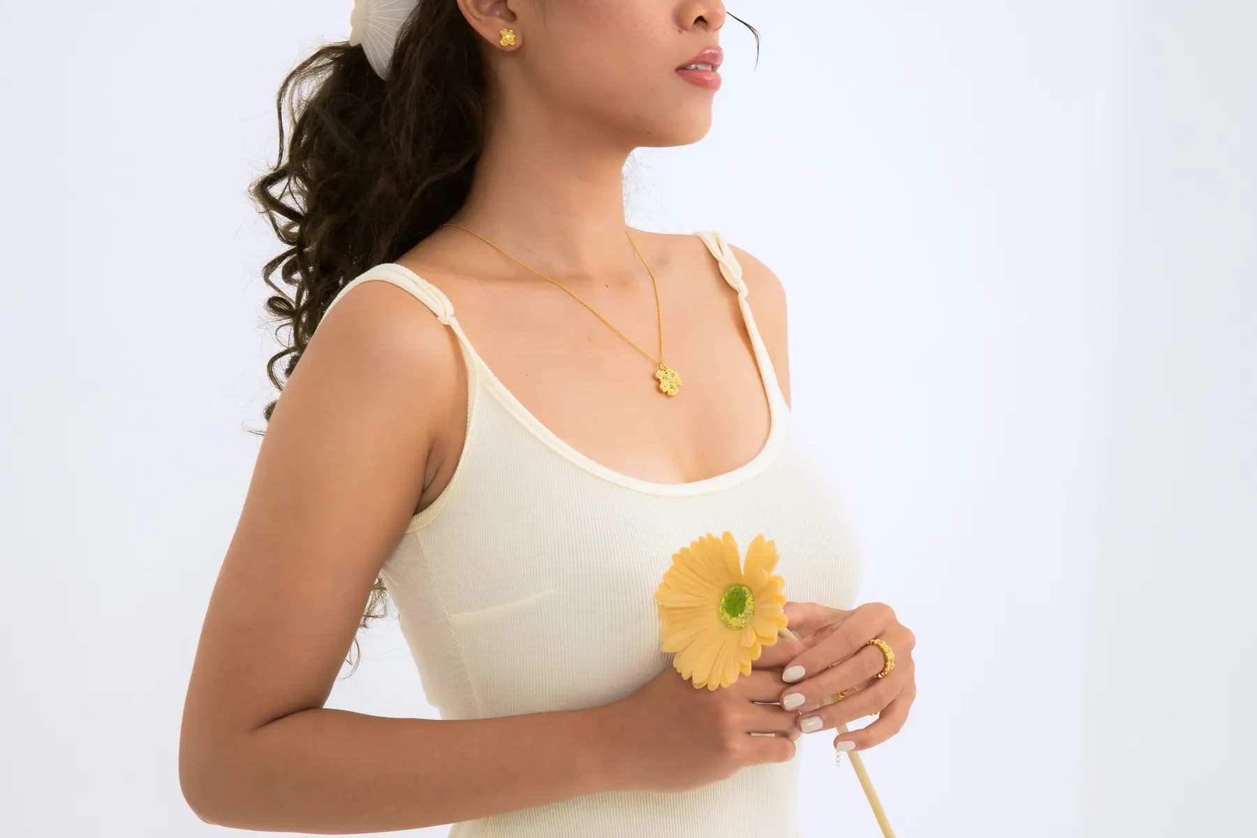 Model in a cream top holding a yellow flower, wearing a gold pendant necklace
