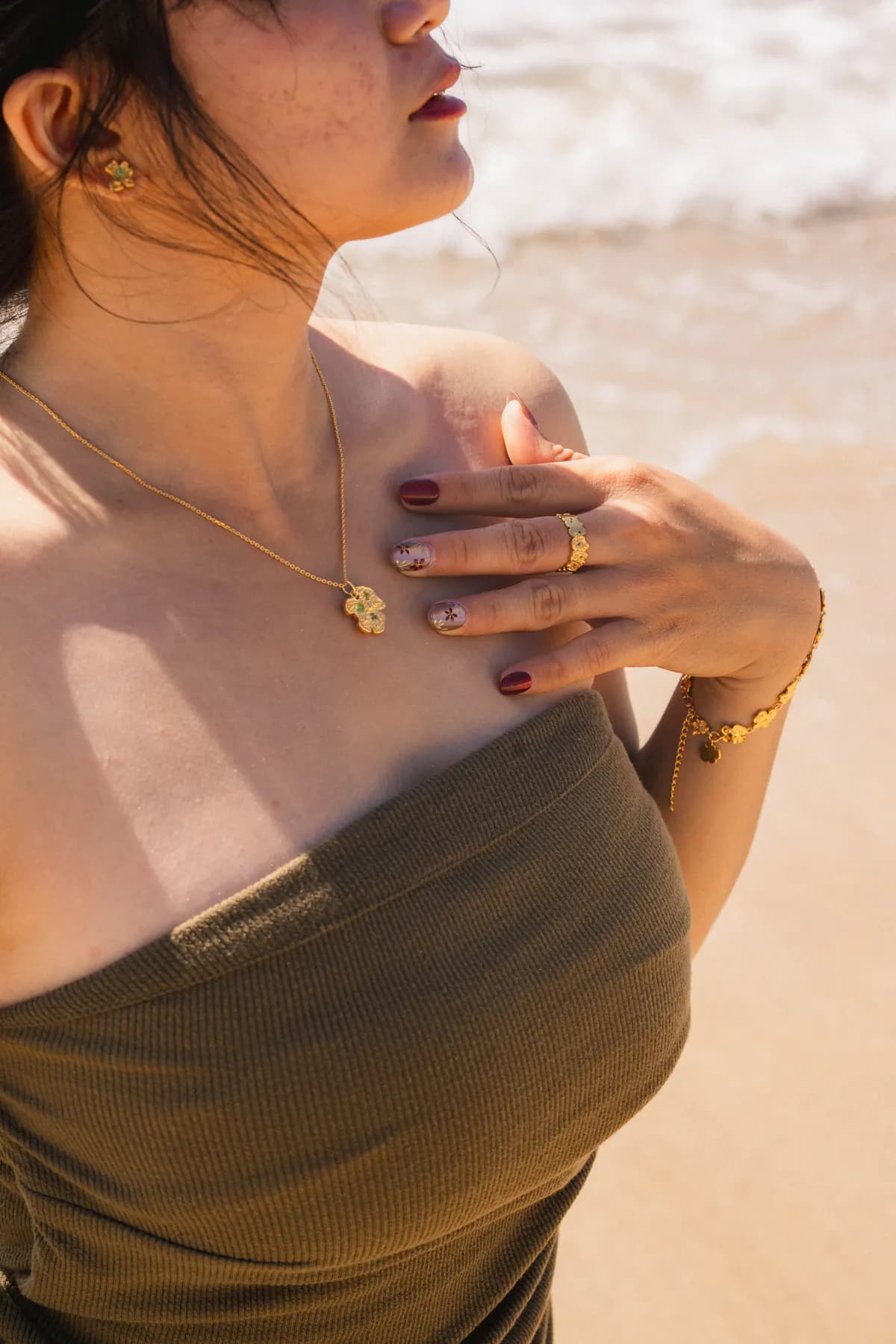 Woman in an olive bandeau on the beach wearing a flower pendant and rings